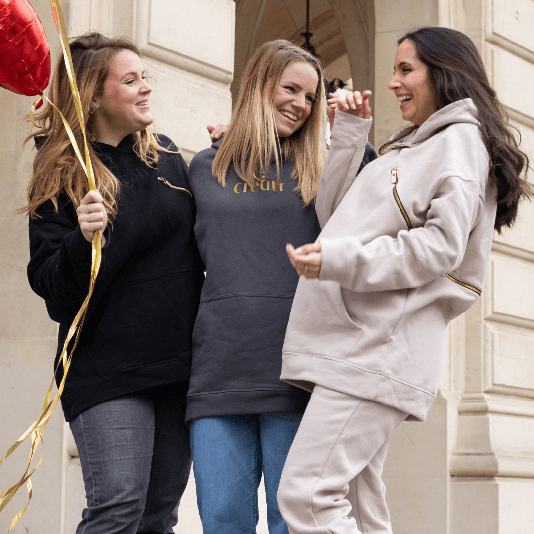 Drei lachende Frauen in creätr Outfits - Umstandshosen, Jeans, Jogger, Hoodie mit Reisverschluss